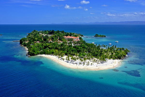 Aerial view of a small palm-covered Dominican island ringed by white sand and turquoise reef water